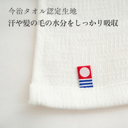白いタオル生地に縫い付けられた今治タオルのタグのアップ。「今治タオル認定生地」「汗や髪の毛の水分をしっかり吸収」の文字が入っている